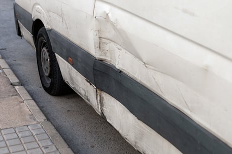 Dented and scratched side panel of a white commercial van