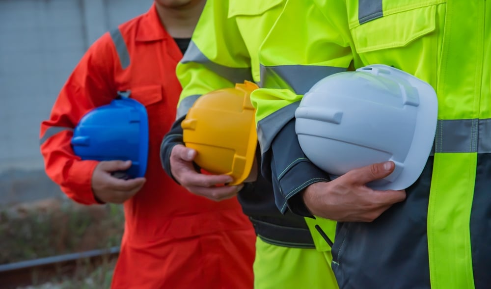 Three industrial workers in high-visibility gear holding hard hats for workplace bodily injury coverage.